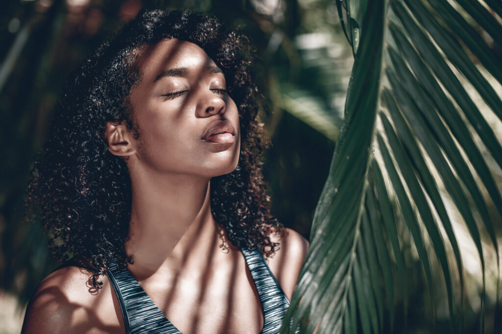 An African American woman under a palm leaf with her eyes closed