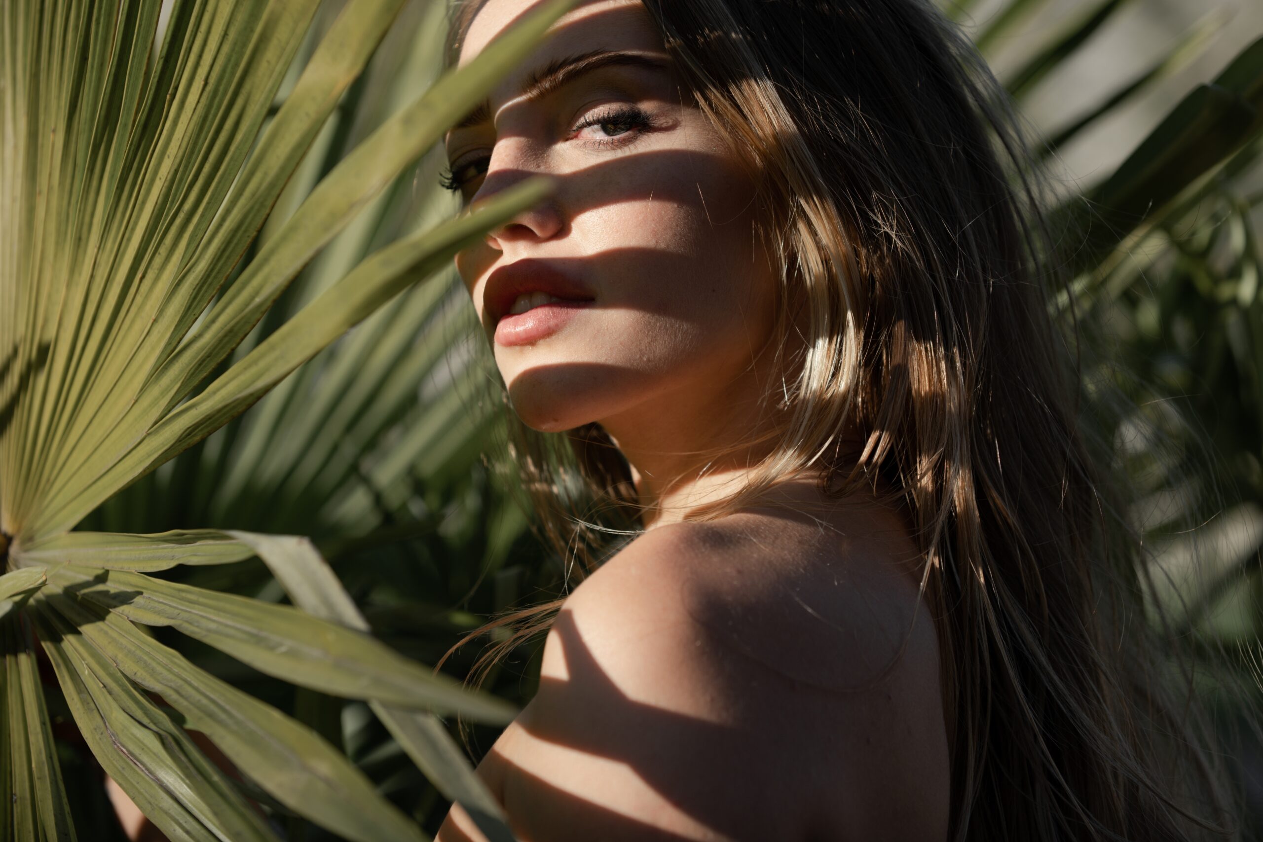 A brunette woman standing behind a palm leaf.