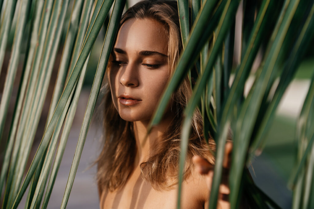 A blonde woman looking out through a palm leaf