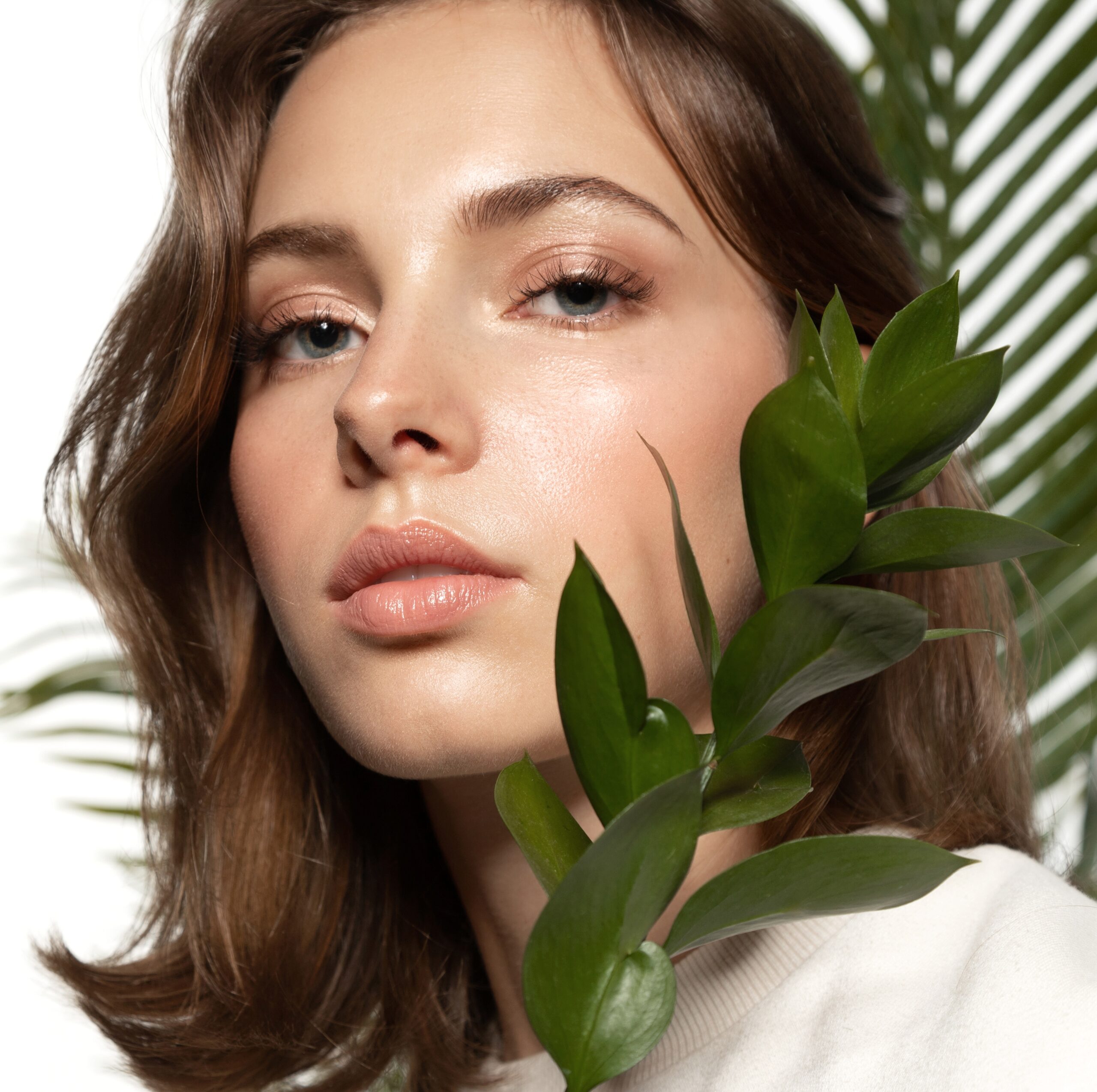 A brunette woman standing next to a palm leaf.