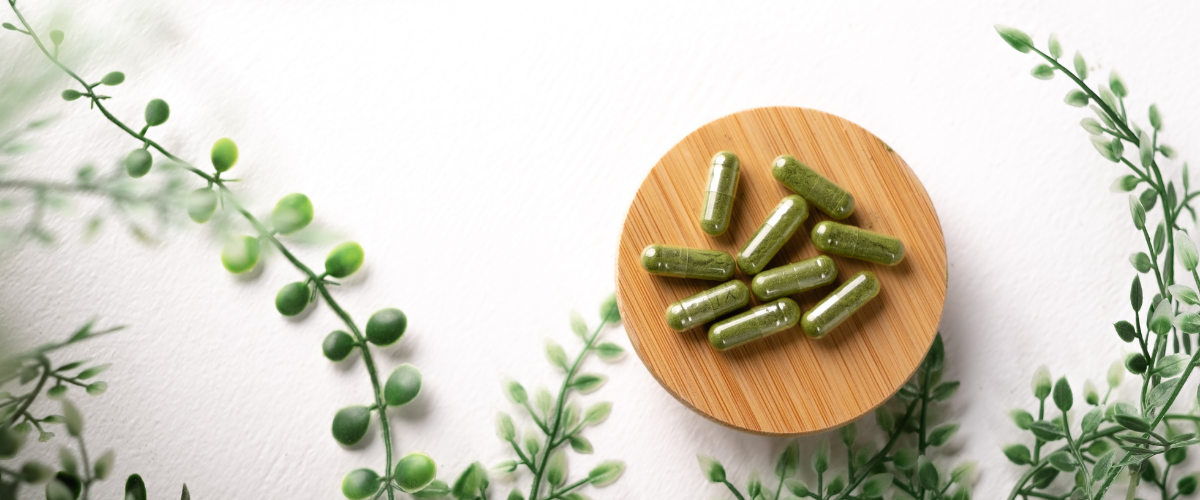 Images of green supplements sitting on a wooden circle with green plants around the supplements