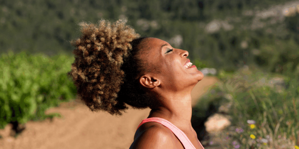 A side profile of a woman outside with eyes closed looking up to the sky and smiling not worrying about aging skin