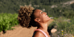 A side profile of a woman outside with eyes closed looking up to the sky and smiling not worrying about aging skin