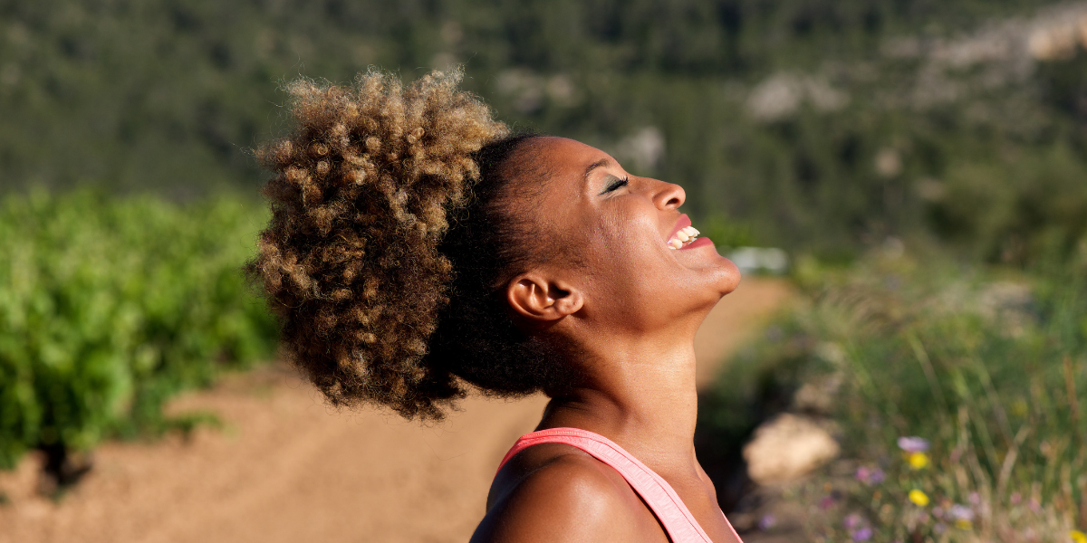 A side profile of a woman outside with eyes closed looking up to the sky and smiling not worrying about aging skin