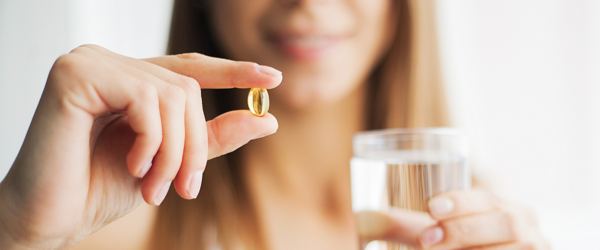 Woman smiling holding a vitamin b6 tablet between her fingers